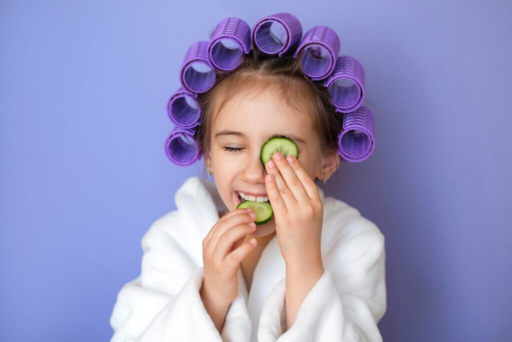 Children pamper party in London. Girl holding cucumber on eye and eating cucumber