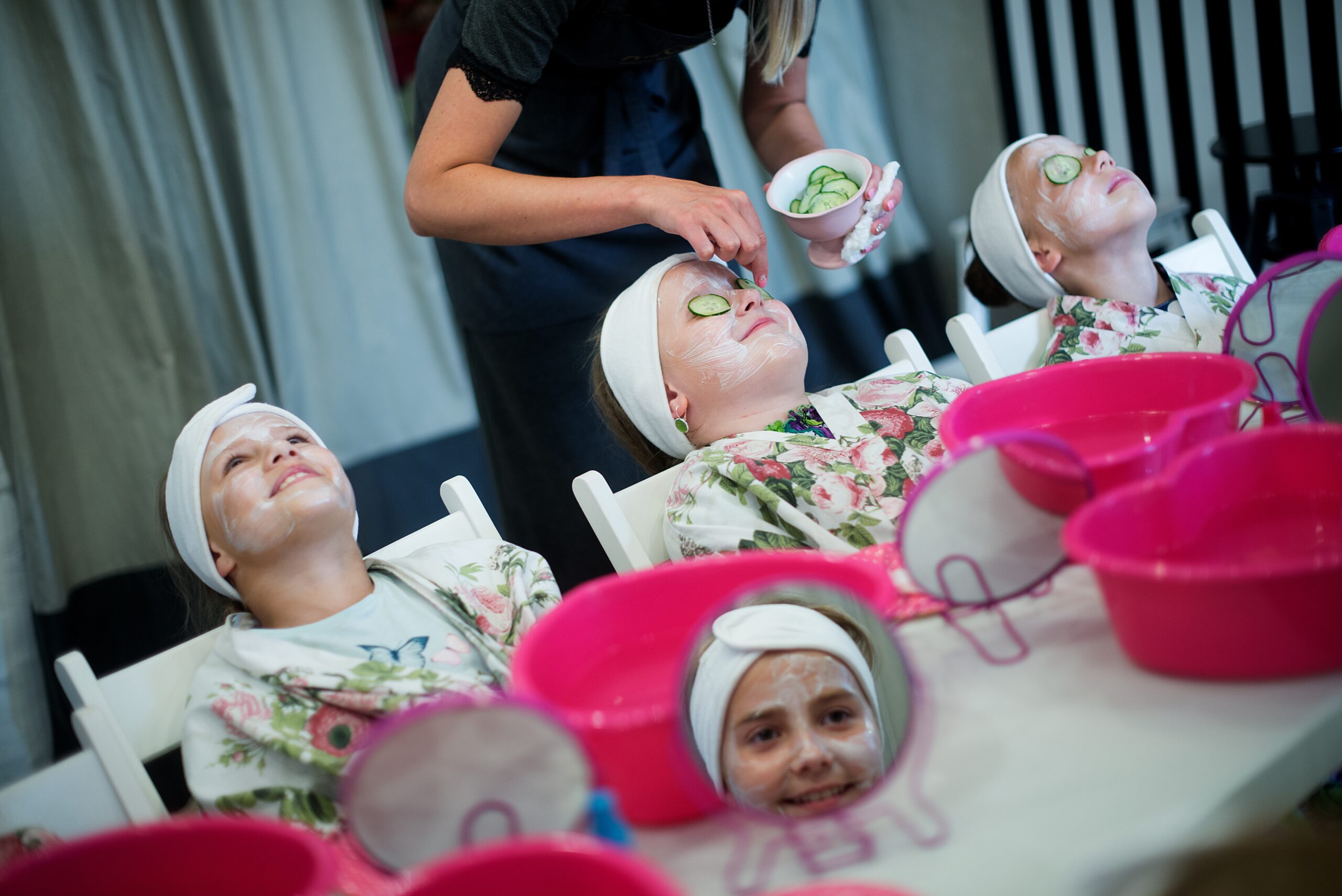 Person pampering children by placing cucumbers on their eye lids. For a pampering party for children